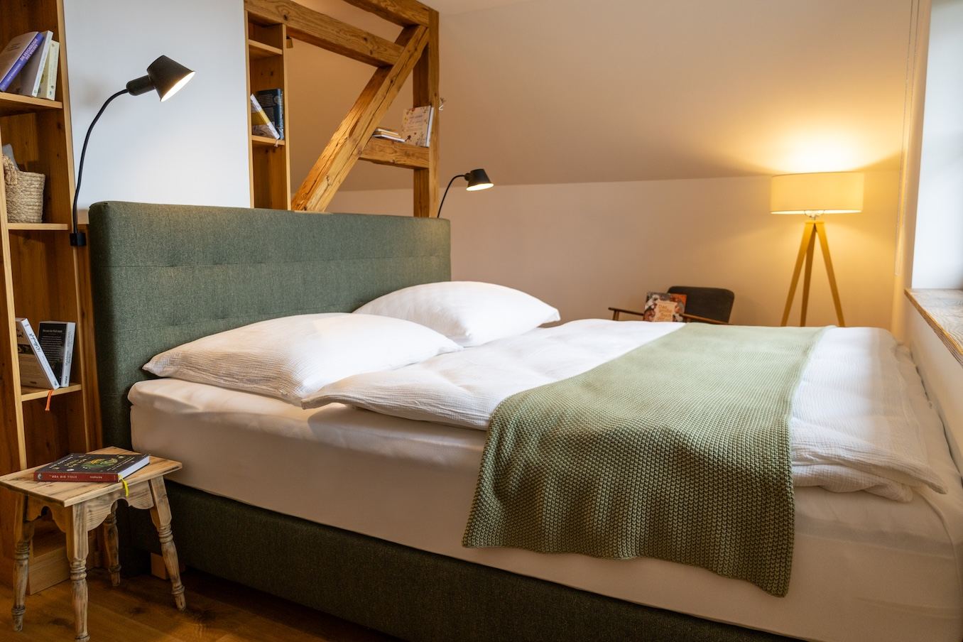 Schlafzimmer mit grünem Polsterbett, Leselampen und Holzregal