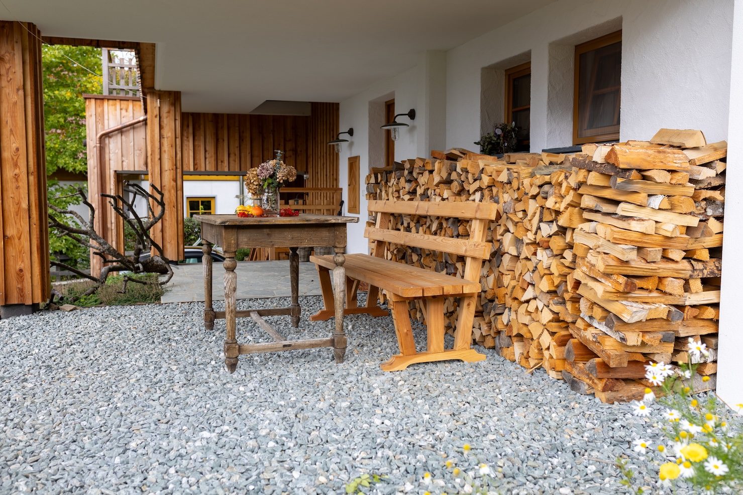 Terrasse mit altem Holztisch, Bank und aufgeschichtetem Brennholz